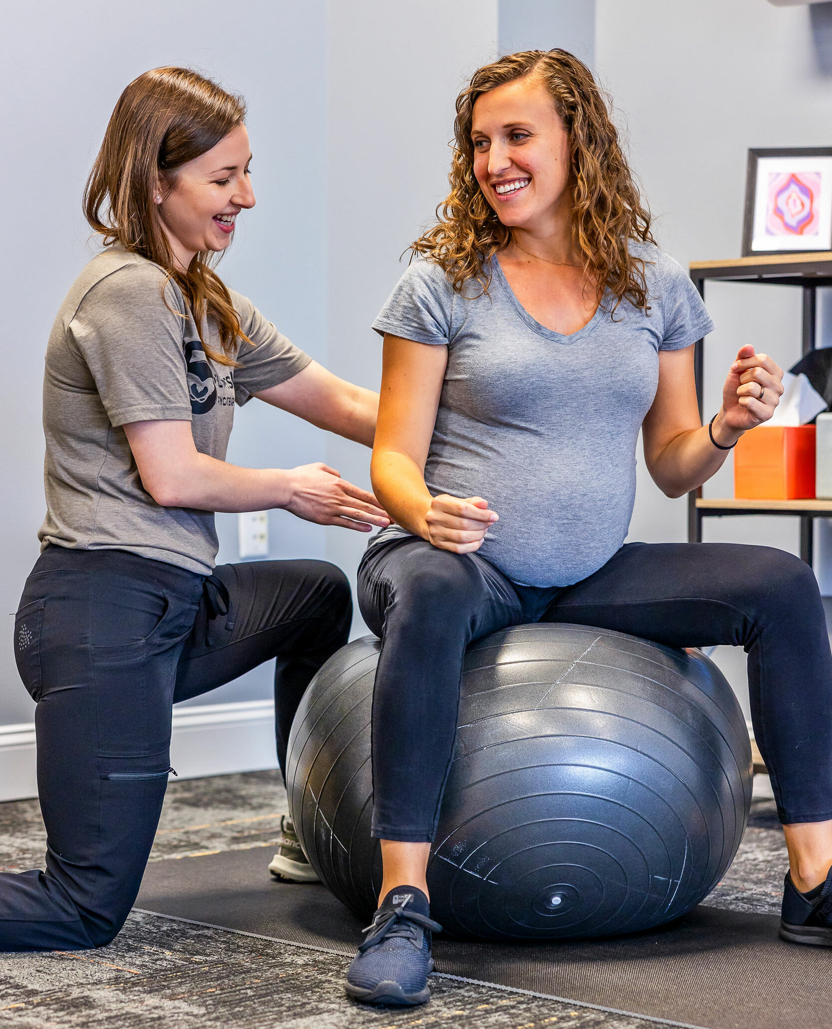 pregnant woman sitting on exercise ball with trainer